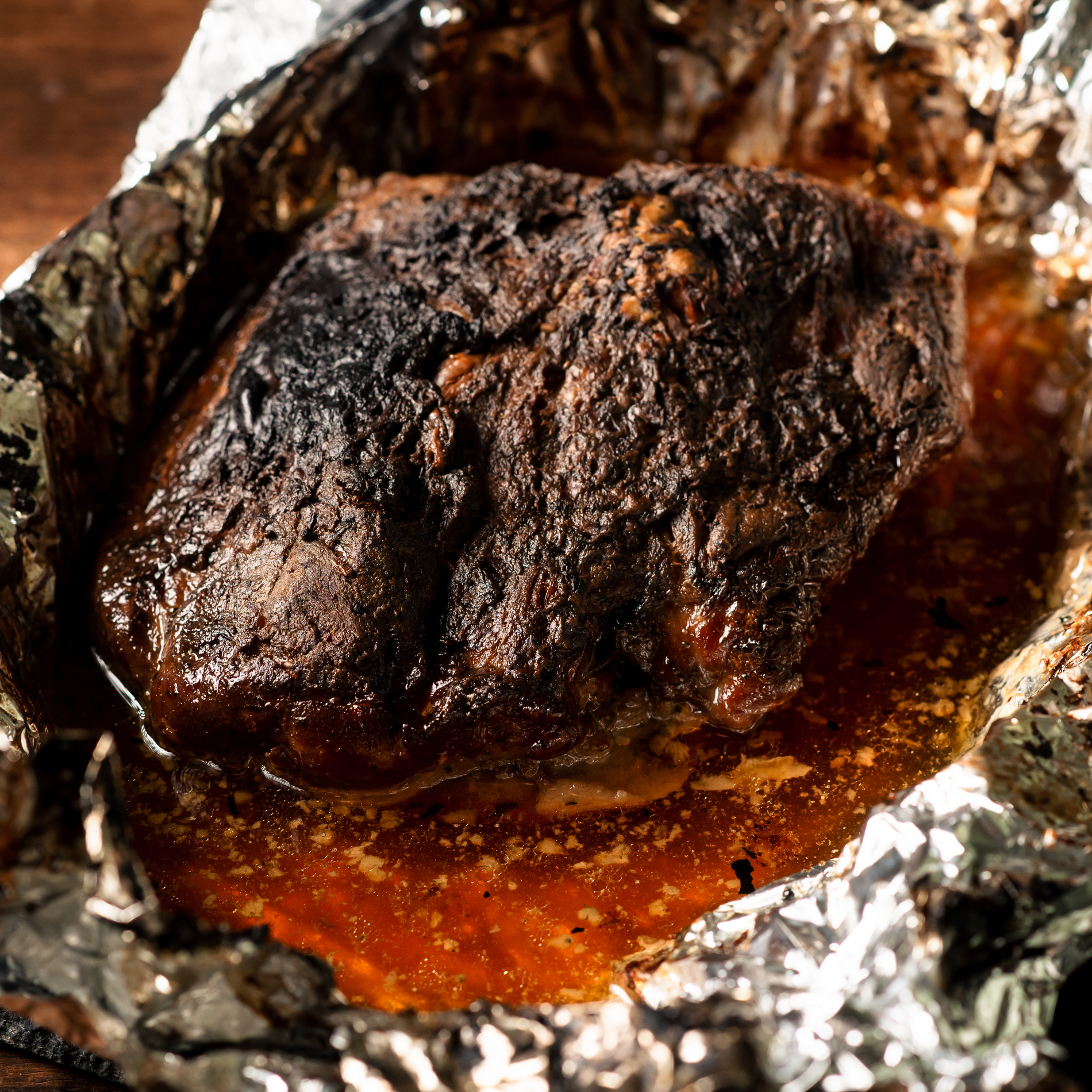 A large piece of baked meat with spices wrapped in foil in the oven.
